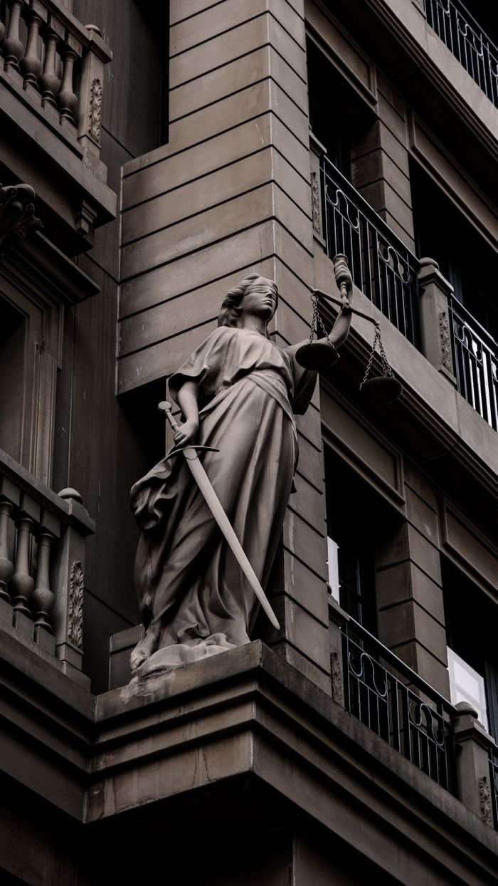 A sculpture of Lady Justice with a sword and scales on a city building's facade.